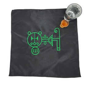 May include: A black cloth with a green sigil embroidered on it. The sigil is a circle with a cross inside, and a key-like shape extending from the right side. The number "III" is inscribed below the circle.