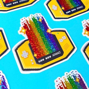 May include: A sticker of a yellow Game Boy Advance with a rainbow pixelated design and the text "Gay Boy Advance".