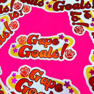 May include: A sticker with a white background and a yellow, red, and orange gradient design. The sticker says "Gape Goals!" with a red rose and pink stars on either side.