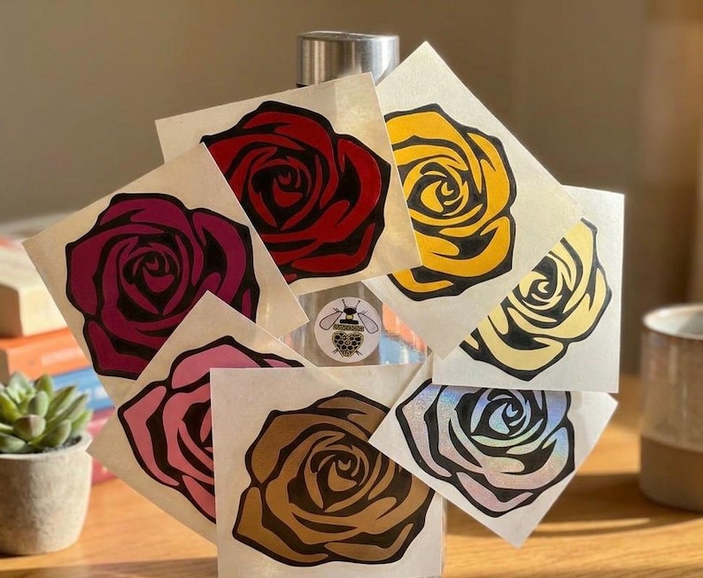 Puede incluir: Una colecci&oacute;n de pegatinas de rosas en varios colores, incluyendo rojo, amarillo, rosa y marr&oacute;n. Cada pegatina presenta un dise&ntilde;o detallado de rosa con contornos negros. Las pegatinas se muestran sobre una superficie transparente.