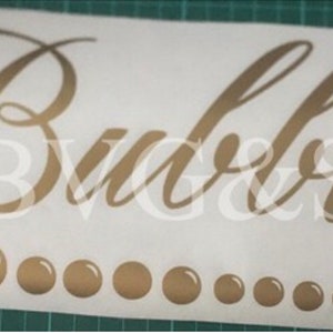 May include: A white sticker with the word "Bubbles" in elegant gold script. Below the word are a series of gold bubble graphics, decreasing in size from left to right. The sticker is on a green cutting mat.