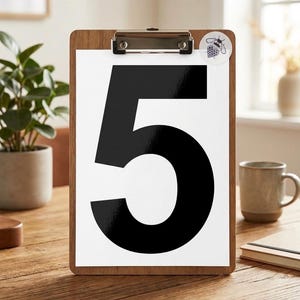Op de afbeelding: Een houten clipboard met een wit papier met een groot zwart cijfer 5. Een kleine ronde sticker met een bijengrafiek is bevestigd. De clipboard ligt op een houten tafel.