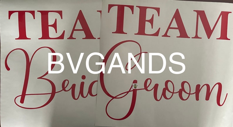 K&ouml;nnte beinhalten: Zwei wei&szlig;e Bl&auml;tter mit rotem Text. Auf einem Blatt steht "TEAM Bride" in einer kursiven Schrift. Auf dem anderen steht "TEAM Groom" in einer &auml;hnlichen Schrift. Das Wort "BVGANDS" steht in wei&szlig;en Blockbuchstaben.