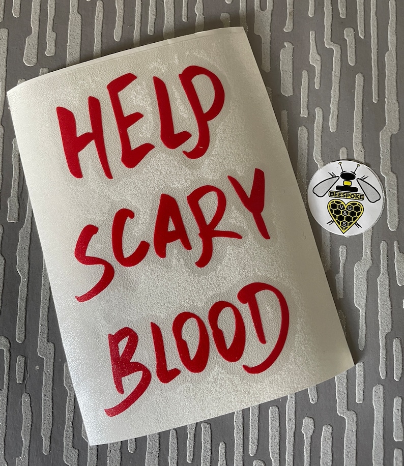 May include: A white sticker with the words "HELP SCARY BLOOD" in red, handwritten-style font. A round sticker with a bee design and the word "BEESPOKE" is also visible.