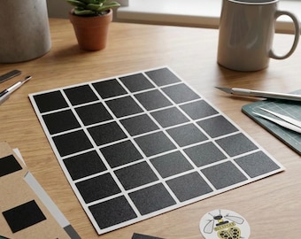 Può includere: Un foglio di adesivi quadrati neri con linee a griglia bianche, insieme a un piccolo adesivo rotondo con un disegno di ape. Gli adesivi sono su una scrivania di legno con una tazza, una pianta e strumenti artigianali.