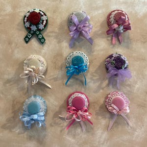 May include: Nine miniature hats with various colors and designs. The hats are made of fabric and have lace trim. Some of the hats have ribbons and bows.