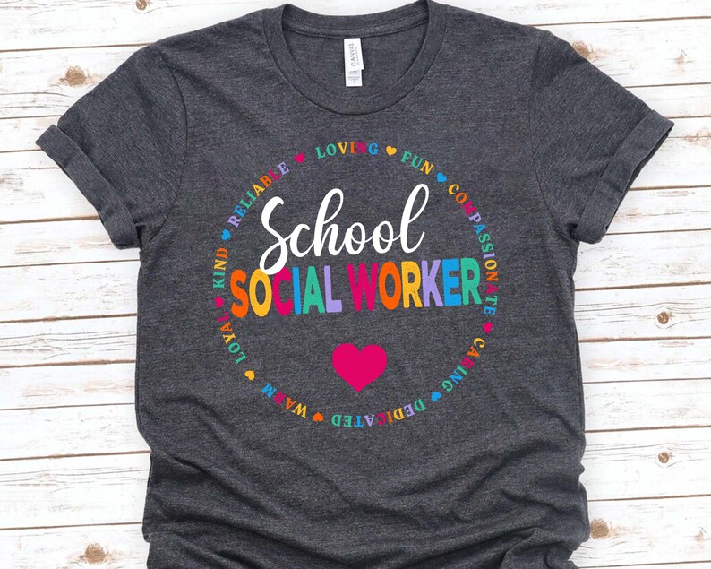 May include: A dark grey t-shirt with a circle design featuring the words "School Social Worker" in rainbow colors. The circle is surrounded by words describing positive qualities, such as "kind", "reliable", "loving", "fun", "compassionate", "caring", "dedicated", "warm", "loyal", and "passionate".