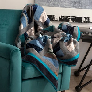 Può includere: Una poltrona blu turchese con una trapunta patchwork realizzata in tessuto blu, grigio e bianco. La trapunta presenta un motivo geometrico ed è ripiegata sullo schienale della poltrona.