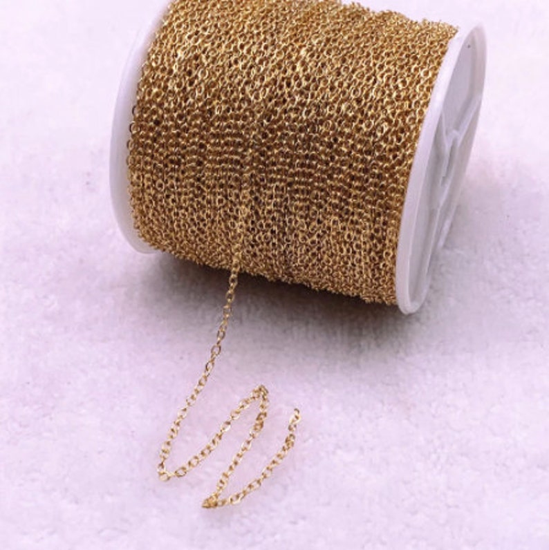 K&ouml;nnte beinhalten: Eine Spule mit goldfarbener Kette, wahrscheinlich f&uuml;r die Schmuckherstellung, wird vor einem weichen, hellen Hintergrund gezeigt. Die Kette ist eng auf eine wei&szlig;e Spule gewickelt, wobei ein kleines St&uuml;ck Kette herausragt. Die Kettenglieder sind klein und gleichm&auml;&szlig;ig.