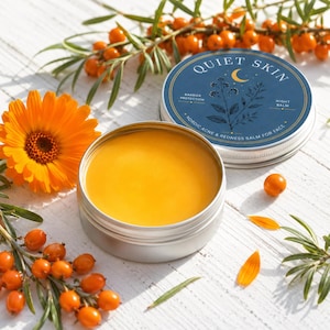 Puede incluir: Una lata redonda de plata que contiene un bálsamo amarillo suave, con una tapa etiquetada como Quiet Skin, Barrier Protection, Night Balm y Nordic Acne & Redness Balm for Face. La lata está rodeada de flores de caléndula y bayas de espino amarillo.
