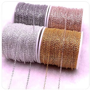 Puede incluir: Cuatro carretes de cadena, cada uno en un color diferente: plata, oro, oro rosa y plata más claro. La cadena está enrollada alrededor de los carretes, que son blancos.