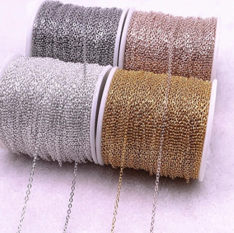 K&ouml;nnte beinhalten: Nahaufnahme von vier Spulen mit Ketten in Silber, Gold, Ros&eacute;gold und Gunmetal-Grau. Die Ketten sind fein und filigran, geeignet f&uuml;r die Schmuckherstellung. Die Spulen sind wei&szlig;, die Kette ist um sie gewickelt.