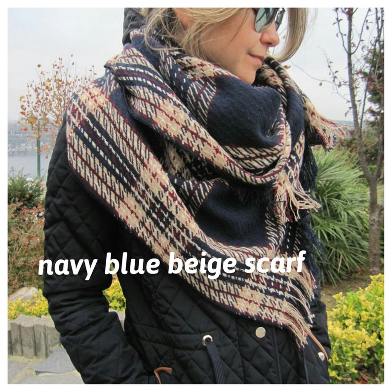 May include: Navy blue, beige, and red plaid scarf with fringe. The scarf is folded and draped around a person's neck.
