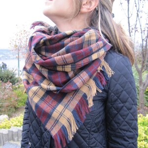 May include: A woman wearing a black quilted jacket with a red, blue, and tan plaid scarf with fringe.