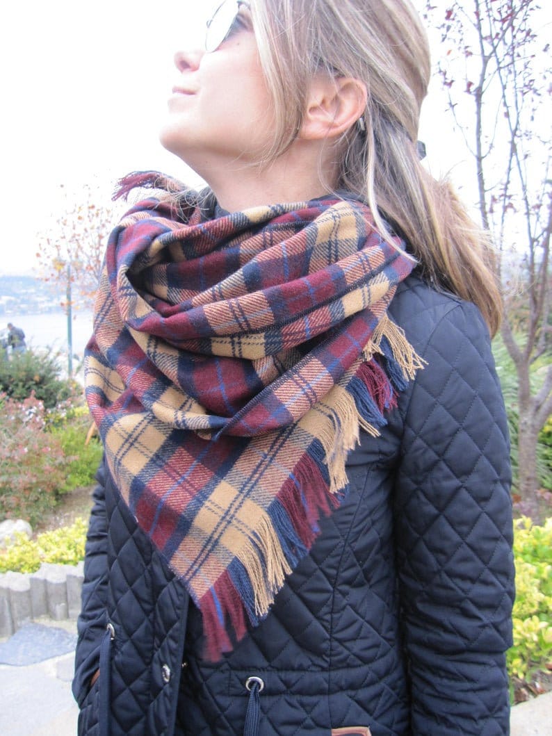 May include: A woman wearing a black quilted jacket with a red, blue, and tan plaid scarf with fringe.