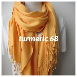 May include: A yellow scarf with fringe. The scarf is folded and draped around a mannequin's neck. The text "turmeric 68" is printed on the scarf.