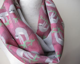 May include: A pink and gray infinity scarf with a repeating pattern of sloths on branches. The sloths are white and have black eyes.