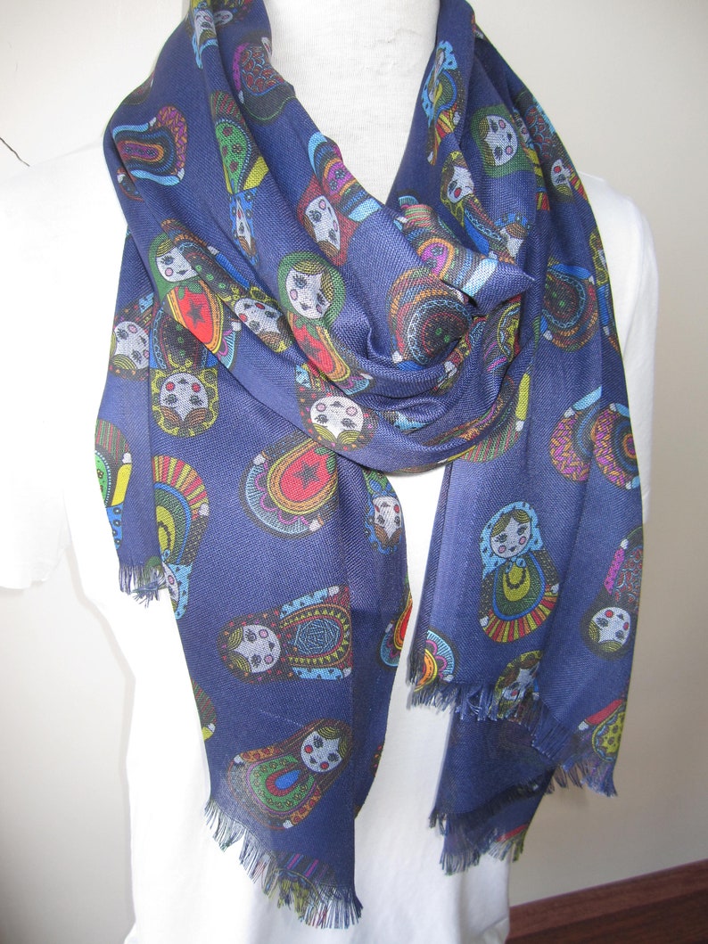 May include: A navy blue scarf with a fringe border features a repeating pattern of colorful Russian nesting dolls.
