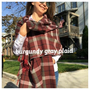 May include: Burgundy, gray, and pink plaid scarf with fringe tassels. The scarf is wrapped around a person's neck and shoulders.