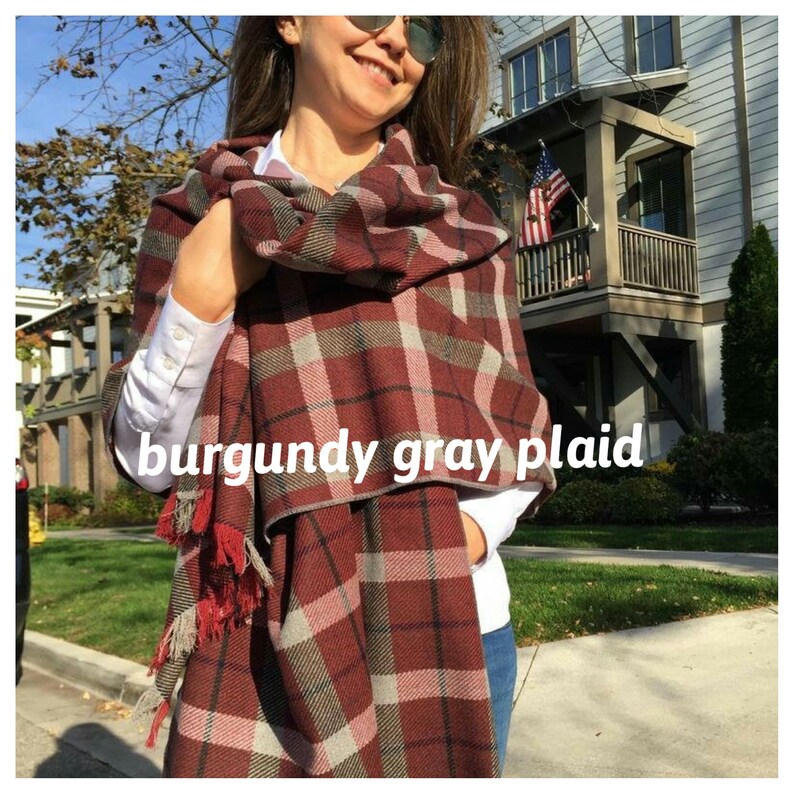 May include: Burgundy, gray, and pink plaid scarf with fringe tassels. The scarf is wrapped around a person's neck and shoulders.