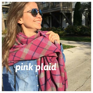May include: A woman wearing a pink and blue plaid scarf. The scarf is wrapped around her neck and tied in a knot at the front. The scarf has a soft, fuzzy texture.