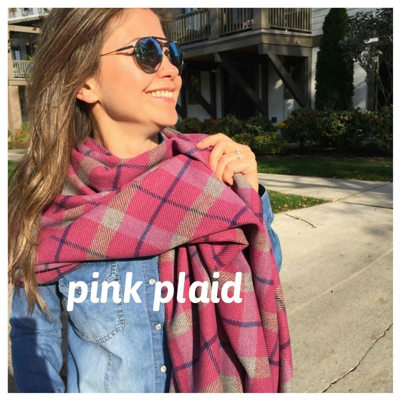 May include: A woman wearing a pink and blue plaid scarf. The scarf is wrapped around her neck and tied in a knot at the front. The scarf has a soft, fuzzy texture.