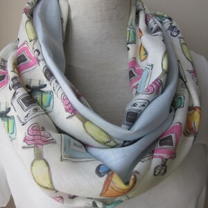 May include: A white infinity scarf with a light blue reverse side. The scarf is printed with a pattern of colorful perfume bottles.