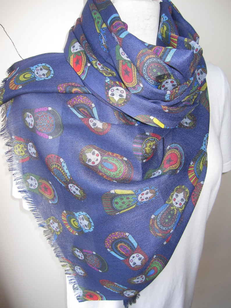 May include: A navy blue scarf with a fringed edge features a repeating pattern of colorful Russian nesting dolls.