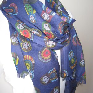 May include: A navy blue scarf with a colorful pattern of Russian nesting dolls. The scarf has a fringed edge.