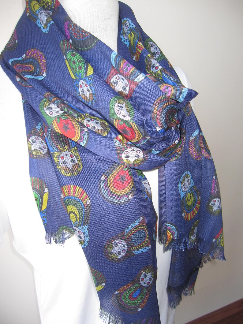 May include: A navy blue scarf with a colorful pattern of Russian nesting dolls. The scarf has a fringed edge.