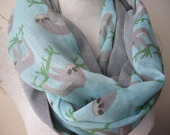 May include: A light blue and gray infinity scarf with a sloth print. The scarf features sloths hanging from branches on a light blue background. The reverse side of the scarf is gray.
