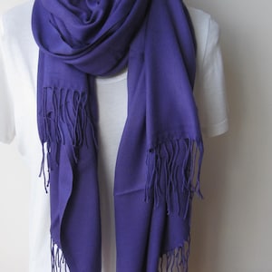 May include: A purple pashmina scarf with fringe. The scarf is draped over a white shirt.