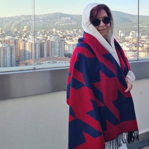 May include: A woman wearing a white hooded sweatshirt and a red and blue star patterned scarf. The scarf has a fringe trim.