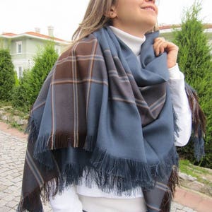 May include: A blue and brown plaid scarf with fringe. The scarf is folded and draped around a person's neck.