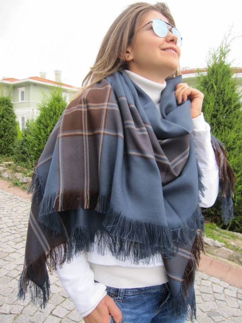 May include: A blue and brown plaid scarf with fringe. The scarf is folded and draped around a person's neck.