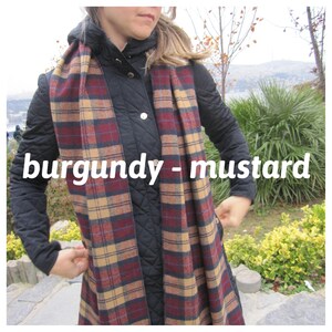 May include: A burgundy and mustard plaid scarf. The scarf is wrapped around the neck of a person wearing a black quilted jacket.