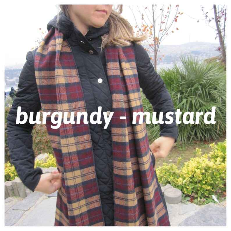 May include: A burgundy and mustard plaid scarf. The scarf is wrapped around the neck of a person wearing a black quilted jacket.