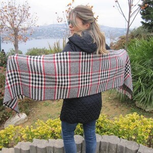 May include: A woman wearing a black jacket and a plaid scarf. The scarf is black, white, and red with a checkered pattern.