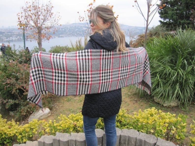 May include: A woman wearing a black jacket and a plaid scarf. The scarf is black, white, and red with a checkered pattern.
