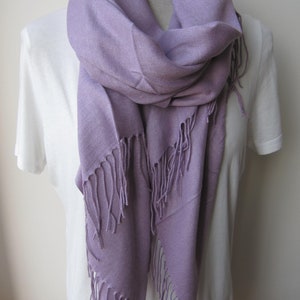 May include: A soft, lavender-colored scarf with fringed edges. The scarf is draped around a white shirt.