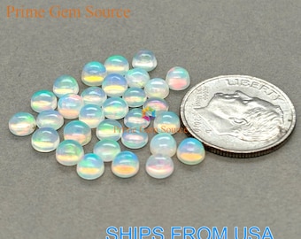Può includere: Una collezione di pietre preziose di opale iridescenti, tagliate a cabochon. Gli opali sono rotondi, con una superficie liscia e lucida, e mostrano un gioco di colori. Una moneta da un quarto di dollaro USA è inclusa per riferimento. Il testo "Prime Gem Source" e "SHIPS FROM USA" sono visibili.