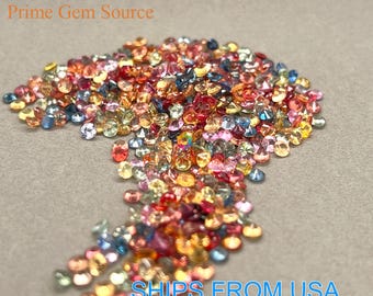May include: A large pile of colorful faceted gemstones, including red, orange, yellow, green, blue, and purple. The gemstones are scattered on a light gray surface.