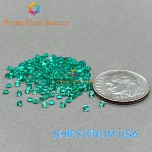 Puede incluir: Un montón de pequeñas piedras preciosas de color verde esmeralda junto a una moneda estadounidense para comparar el tamaño. Las piedras preciosas están dispersas sobre una superficie gris. El texto "Prime Gem Source" es visible.