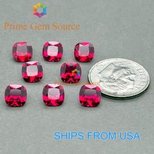 Puede incluir: Ocho gemas de color rojo intenso, con talla cojín, se muestran junto a una moneda de diez centavos estadounidense. Las gemas tienen forma cuadrada con esquinas redondeadas y una superficie facetada. El texto "Prime Gem Source" es visible.