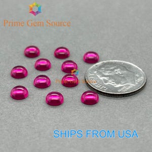 May include: A collection of vibrant, magenta-colored cabochon gemstones. The gemstones are arranged on a gray surface next to a U.S. dime for size comparison. The text "Prime Gem Source" and "SHIPS FROM USA" are visible.