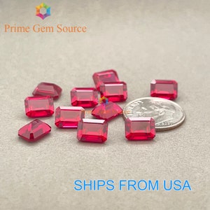 May include: A group of 12 red emerald cut gemstones, some are arranged in a row, with a US dime for scale.