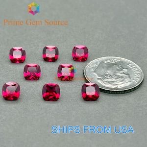May include: Eight cushion-cut, vibrant red gemstones are displayed on a gray surface, alongside a US quarter coin. The gemstones are faceted, reflecting light. The text "Prime Gem Source" is visible in the upper left corner.