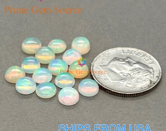 Può includere: Una collezione di pietre preziose di opale iridescenti con una superficie lucida e a cupola. Gli opali sono esposti accanto a una moneta per il confronto delle dimensioni. Le pietre preziose hanno una base bianca lattea con lampi di colore.