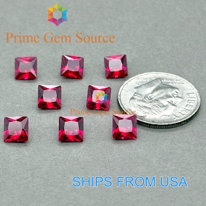 May include: Eight square-cut, vibrant red gemstones are displayed on a gray surface next to a US dime for size comparison. The gemstones are faceted, reflecting light. The text "Prime Gem Source" is visible.