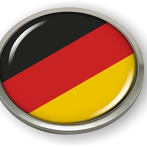 May include: A round button with a glossy finish featuring the German flag. The flag is black, red, and gold with a diagonal stripe.